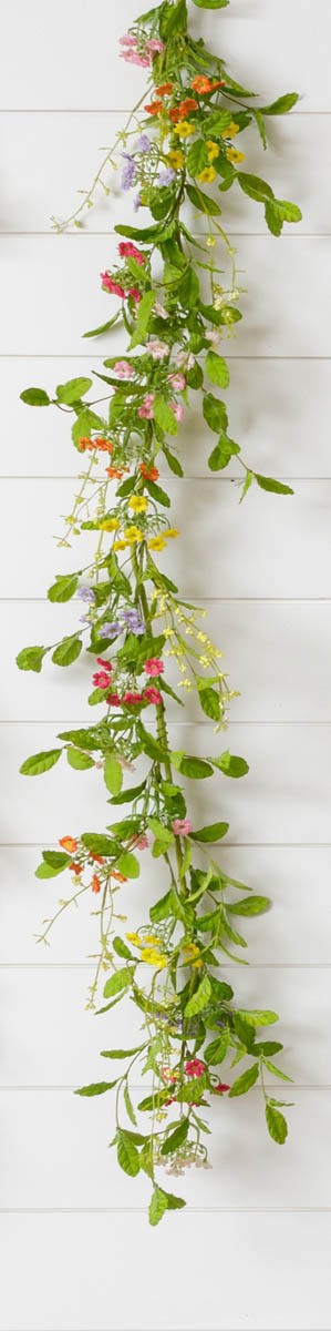 A vertical Garland - Assorted Color Mini Flowers by MyHomeDecor.ca, made of green leaves and mini flowers in assorted colors, including pink, yellow, and purple, is hanging against a white wooden background. The garland appears to be a decorative piece for a wall or doorway.