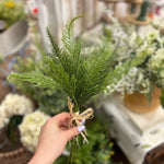 A bundle of genuine MyHomeDecor.ca Fern Bush - Green is tied together with straw-colored raffia ribbon, set against a plain white background. The intricate, feathery foliage of the ferns is vibrant and detailed.