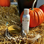 A display features an orange pumpkin, a metal canister of MyHomeDecor.ca Fall Exclusive Package Deal - 4 Pieces, a small brass bowl with green powder, and a decorative shell string of wooden beads. Arranged on a bed of straw, this setup captures an autumnal setting perfect as a host gift.