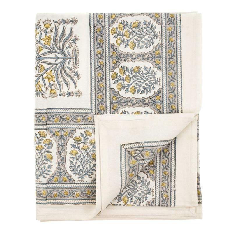 Introducing the Summer Tablecloth Cambria by MyHomeDecor.ca—a beautifully crafted cloth showcasing an intricate floral pattern of blue and yellow flowers. The design, reminiscent of traditional block printing, features symmetric, framed sections and vine-like elements on a pristine white background. Partially unfolded to display both sides of the pattern, it is perfect for adorning farmhouse tables.