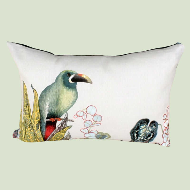 The image features a decorative pillow with an artistic print. It depicts a green bird with a yellow beak perched beside red-berried plants, and a smaller black and white bird on the ground to the right. The background is light-colored, emphasizing the detailed artwork of the birds and flora. This design could be discussed in the context of home decor, illustration styles, or product design.