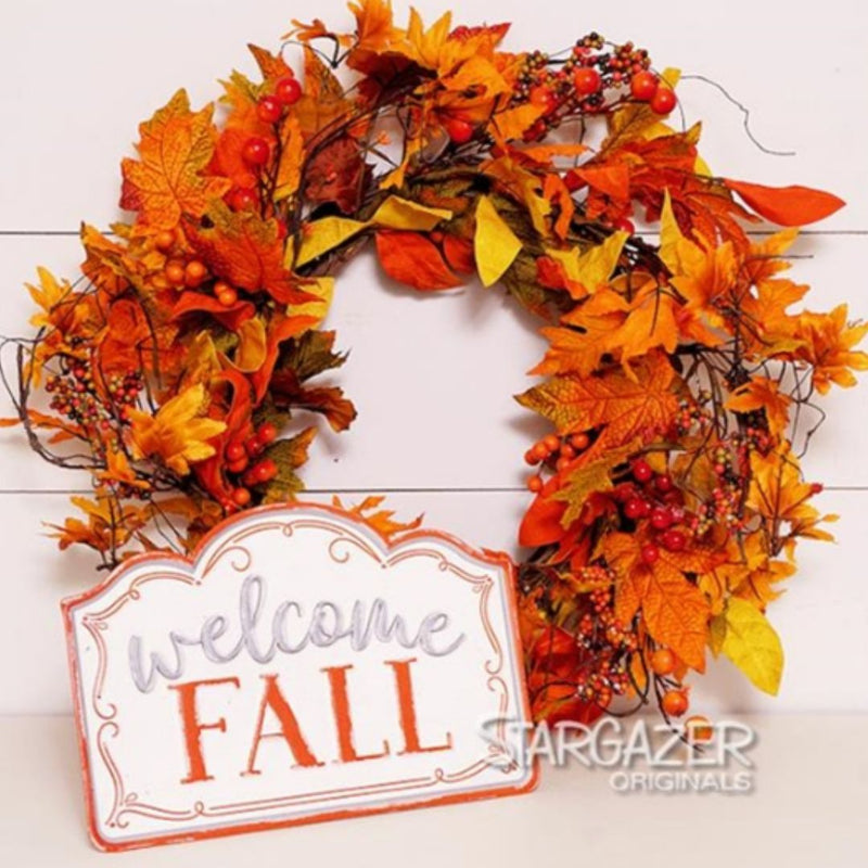 A fall-themed wreath made of orange, yellow, and red leaves, along with red berries and twigs, is displayed against a white wooden background. Attached to the wreath is a small white and orange metal sign that reads "welcome FALL" in orange letters. The bottom right says "MyHomeDecor.ca".