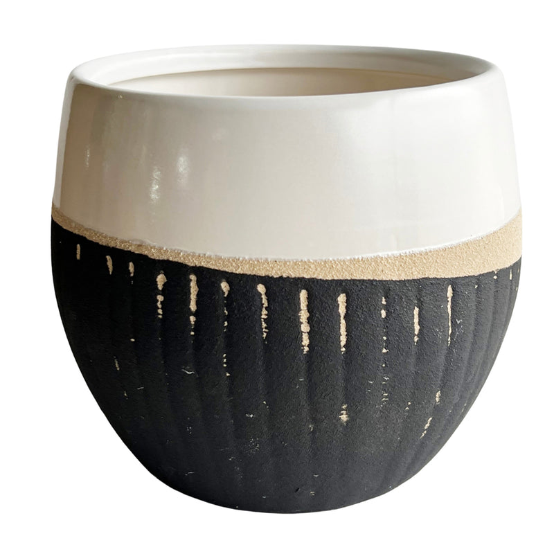 The Large Jennilyn Ceramic Round Vase - Two Tone by MyHomeDecor.ca features a two-tone design. The top half is a smooth, glossy white, while the bottom half is a textured matte black finish with vertical beige streaks. This 6" dia pot has a wide, round shape and an open top, making it perfect for any decor.