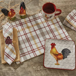 A rustic table setting featuring MyHomeDecor.ca Kingswood placemats, napkins with barn-shaped napkin rings, a red rooster-themed mug, a square plate with a rooster design, and two rooster salt and pepper shakers. All these create a farmhouse touch on a wooden surface with decorative straw for a textured look.