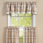 A window with a view of green trees outside, framed by checkered-patterned curtains in shades of beige, brown, and red. The curtains, adorned with a **Lined Layered Valance - Kingswood** from **MyHomeDecor.ca**, are gathered at the top and cover the bottom and sides of the window, letting in light through the center.