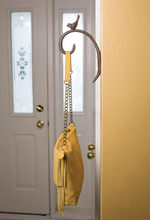 A yellow handbag with a chain strap hangs from a MyHomeDecor.ca Curl Hook with Bird - Brown. The wall is painted yellow, and a white door with frosted glass panels featuring floral designs adds charm to the outdoor space.